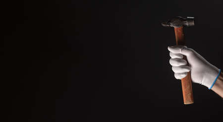 Retro hammer tool with wooden handle in male hand in white glove closeup over black background with copy space for text.の写真素材