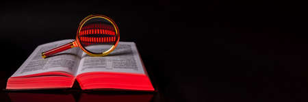 Bible or law code book with magnifying glass for analysis over black background. Banner with space for text.の写真素材