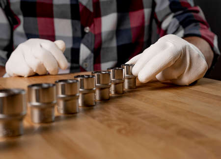 Male hand and line row of metal steel hex sockets or hexagon metal heads on wooden table. Car and home repair metal tool, closeup.の写真素材