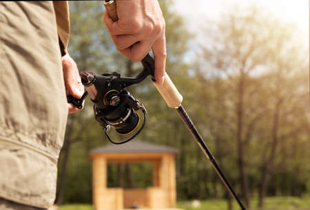 Closeup hands holding reel rod and fishing on summer day.