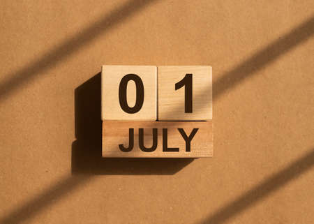 1 July on wooden calendar over brown paper with day light. New month, 1st day.