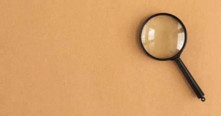 Black magnifying glass over craft brown background with copy space. Search tool concept.の写真素材
