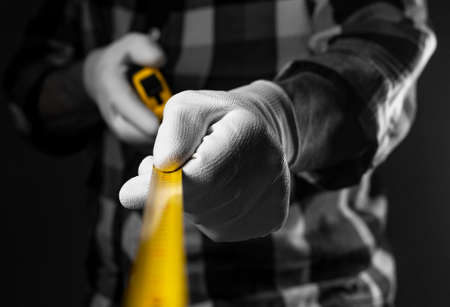 Male hands in white building gloves holding yellow retractable tape measure tool spread to camera, closeup.の写真素材