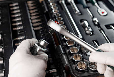 Hands of repairman in gloves close up with metal steel socket ratchet handle over toolbox, POV.