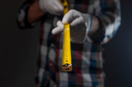 Yellow retractable tape measure tool in hands of man in shirt, closeup.の写真素材