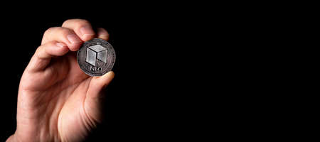 NEO shiny silver coin in male hand over black background with copy space for text.