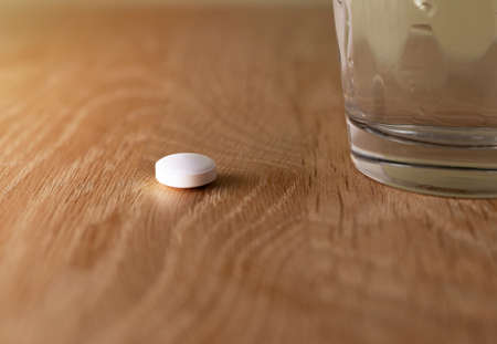 White pill on wooden desk near water glass.の写真素材