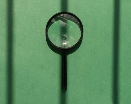 Black magnifying glass over green background with sun light and shadows. Magnifier concept.の写真素材