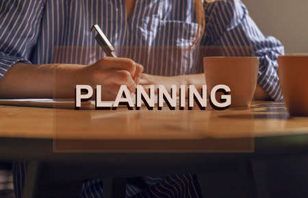Planning concept. Writing notes, plans in notebook on wooden table with coffee cup.