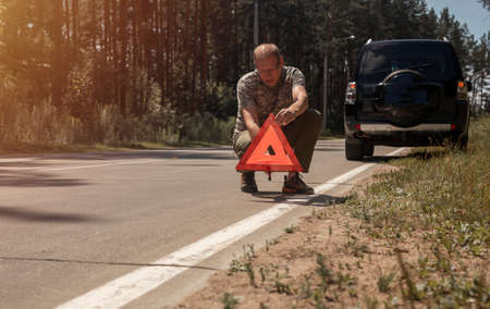 Man putting triangle caution sign on road near broken car.の写真素材