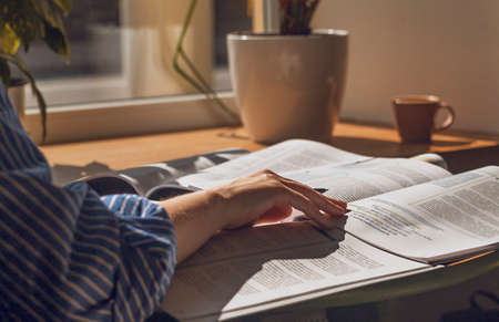 Female hands writing with pen in notebook, taking notes, studying with academic textbook, close up.