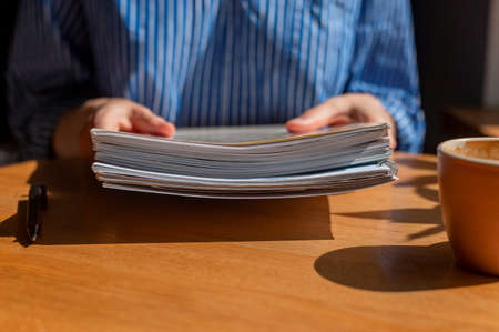 Closeup of women hands with pile of business documents over wooden desk and coffee cup.の写真素材
