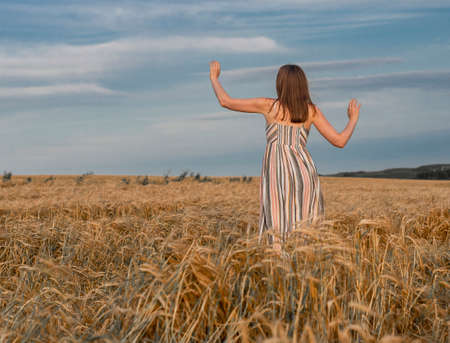 Happy woman running away in gold field in august summer. Concept of freedom and happiness, unity with nature.の写真素材