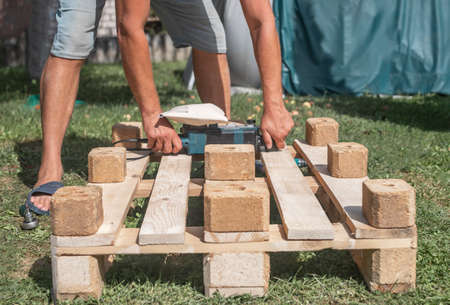 Man with tools work with wooden material, constructing and repairing furniture in nature.の写真素材