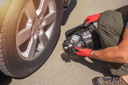 Male hands in glove and portable tire pump for inflating auto wheel. Tyre inflator air compressor with pressure gauge.の写真素材