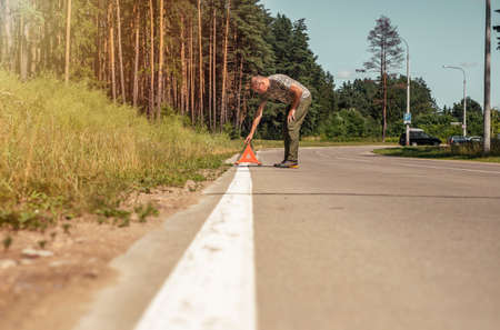 Man putting triangle warning caution sign on road side.の写真素材