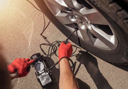 Tire pump inflating car wheel. Tyre inflator in male hands, top view.の写真素材