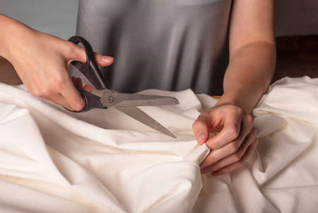 Seamstress cutting cloth with sewing scissors. Dressmaker closeup.
