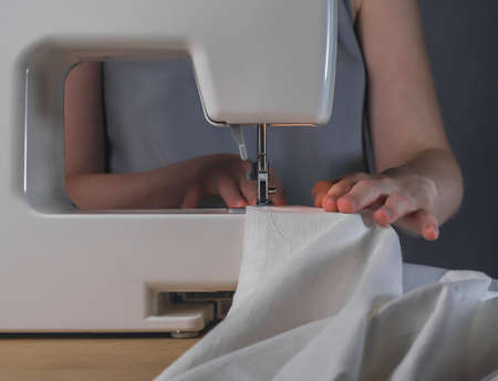 Seamstress hands with linen cloth at sewing machine, working process with organic natural cotton...