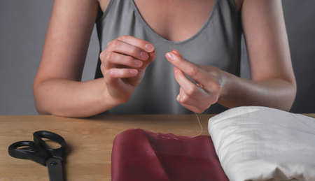 Female hands inserting thread through tiny needle hole for sewing.の写真素材