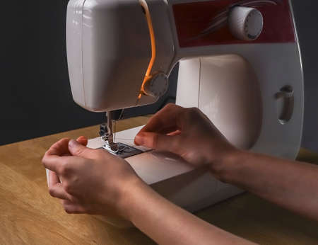 Seamstress hands inserting thread through needle hole in sewing machine, starting work.