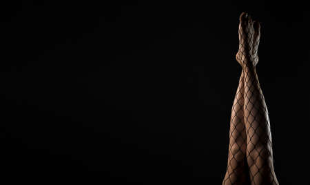 Black fishnet tights on slim legs raised up over black background. Banner with copy space for text.の写真素材
