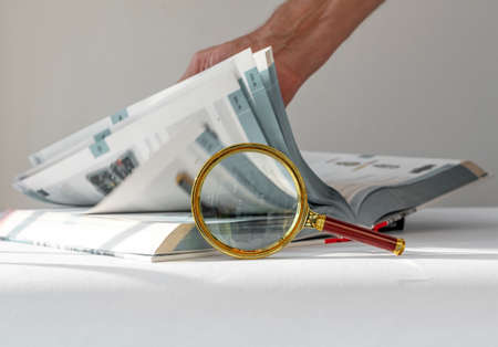 Technical book with turning pages, male hand and magnifying glass. Research and study concept.の写真素材