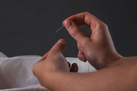 Manual sewing concept. Seamstress hands with needle and cotton cloth, inserting thread through needle hole.の写真素材