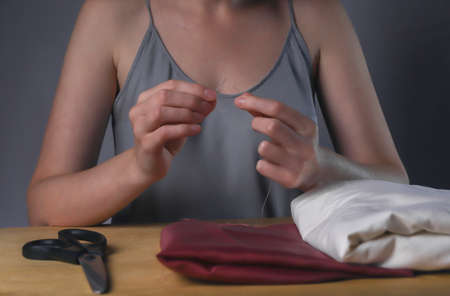 Hands inserting thread through needle hole for sewing at her wood desk.の写真素材