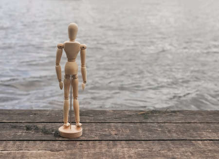 Pensive and sad abstract person on pier near water. Melancholy and loneliness concept.の写真素材