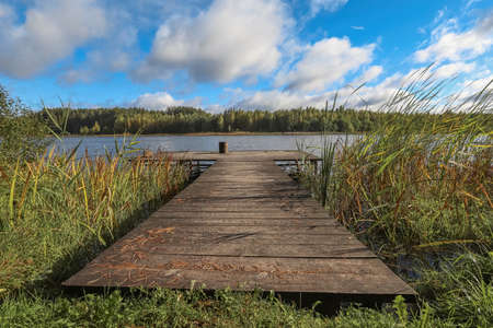 Landscape with wooden long jetty with chair for fishing, lake, forest on horizon and cloudy blue sky in summer.の写真素材