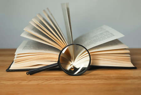 Magnifying glass and open books with turning pages on wood table. Reading and studying concept.の写真素材