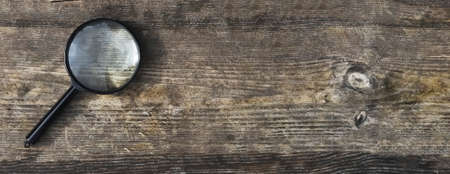 Magnifying lens on wood aged background with copy space for text. Wooden horizontal banner with copyspace.の写真素材