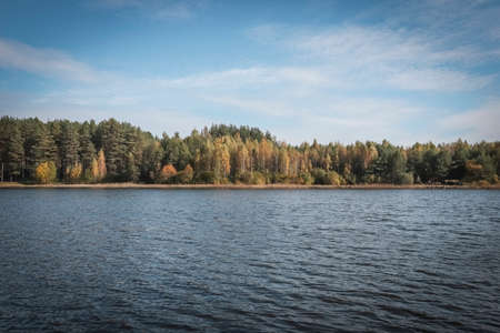 Fall serene landscape with green and yellow woods, its reflection in lake water, clear blue sky...