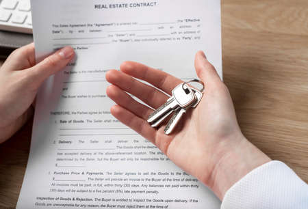 Property keys in hands closeup with real estate contract closeup.