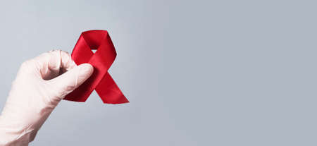 Red ribbon bow for AIDS and HIV awareness day in doctors hands. Medical banner with copy space for text.の写真素材