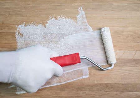 Painting and coloring with white colour wooden surface with paint roller, close up.の写真素材