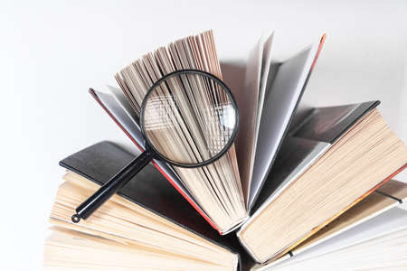 Magnifying glass over open paper book with pages. Concept of academic research, search and studying.