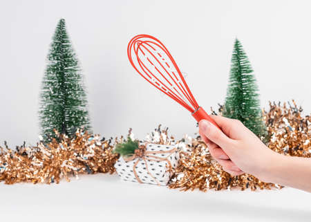 Red whisk tool in hand and Christmas and New Year decoration on background.
