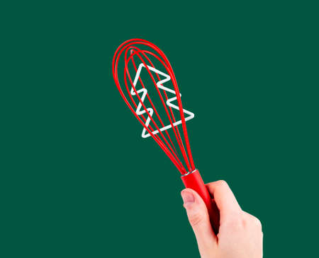 Red whisk tool in hand over green background. Whipping beater with Christmas tree inside.の写真素材