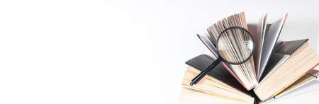 Magnifier over open paper book. Concept of knowledge, research and studying. Banner with copy space.