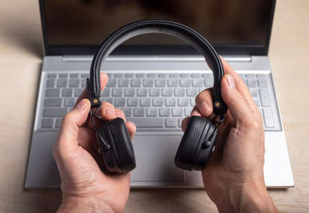 Headphones in hands and laptop. Listening to music and podcast concept.
