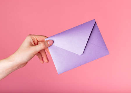 Hand holding purple envelope, gift certificates on pink background. High quality photoの写真素材