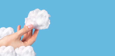 Banner with hand holding cotton cloud at blue sky background. Cloudy weather and meteorology...