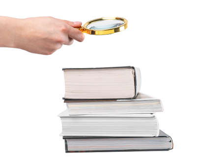 Hand holding magnifying glass over books stack isolated on white background. Research and detailed...