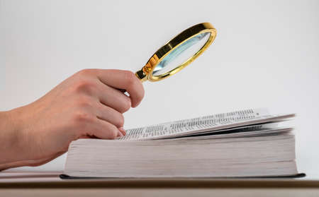 Hand holding magnifying glass over open book. Study, research concept. High quality photo