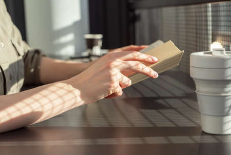 Hands closeup holding book. Woman sitting at cafe table and reading book. Reading literature hobby concept . High quality photoの写真素材