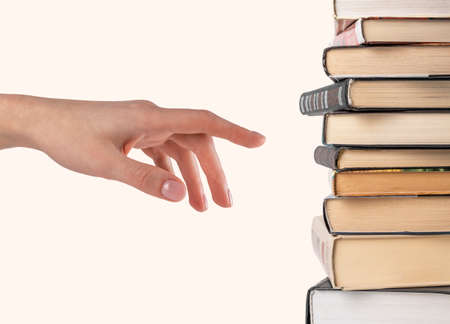 Woman hand selecting or pointing to book from stack isolated on white background. Book choice for reading. High quality photoの写真素材