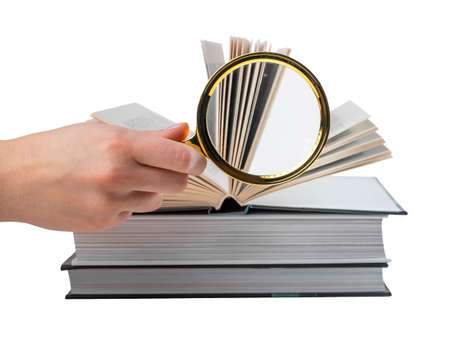 Hand holding magnifying glass near books stack isolated on white background. Information search and analysis concept. High quality photoの写真素材