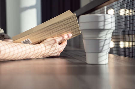 Female hands closeup holding book. Woman sitting in cafe and reading novel. Reading with drinking coffee cup concept. High quality photoの写真素材